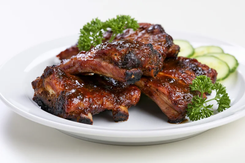 Glazed barbecue pork ribs on a white plate with parsley and cucumber garnish