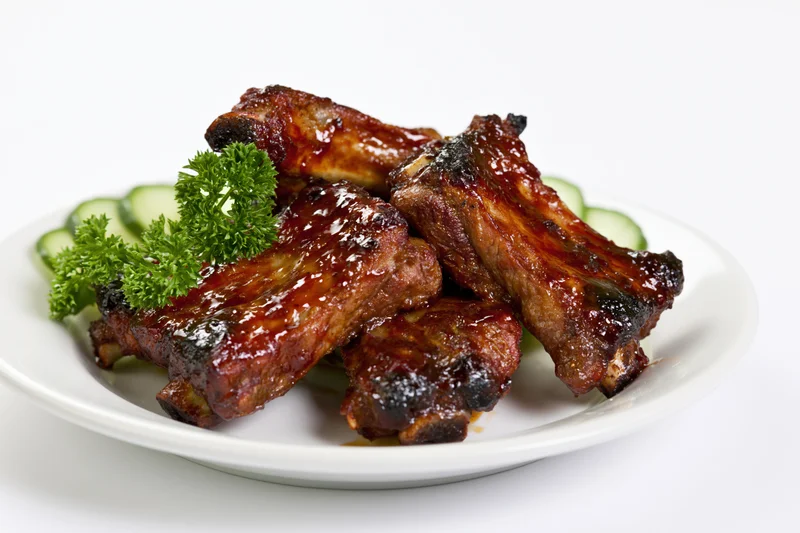 Glazed barbecue pork ribs on a white plate with parsley and cucumber garnish