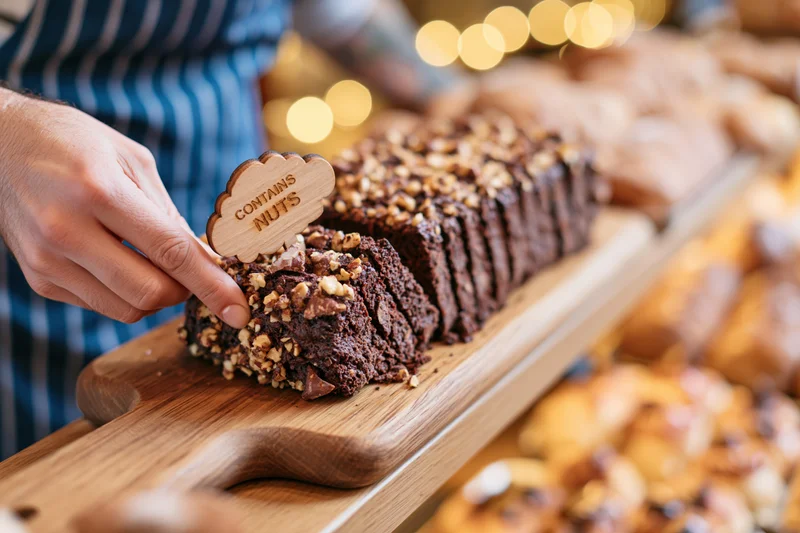 Bakery worker placing wooden allergen label on chocolate nut cake in display case