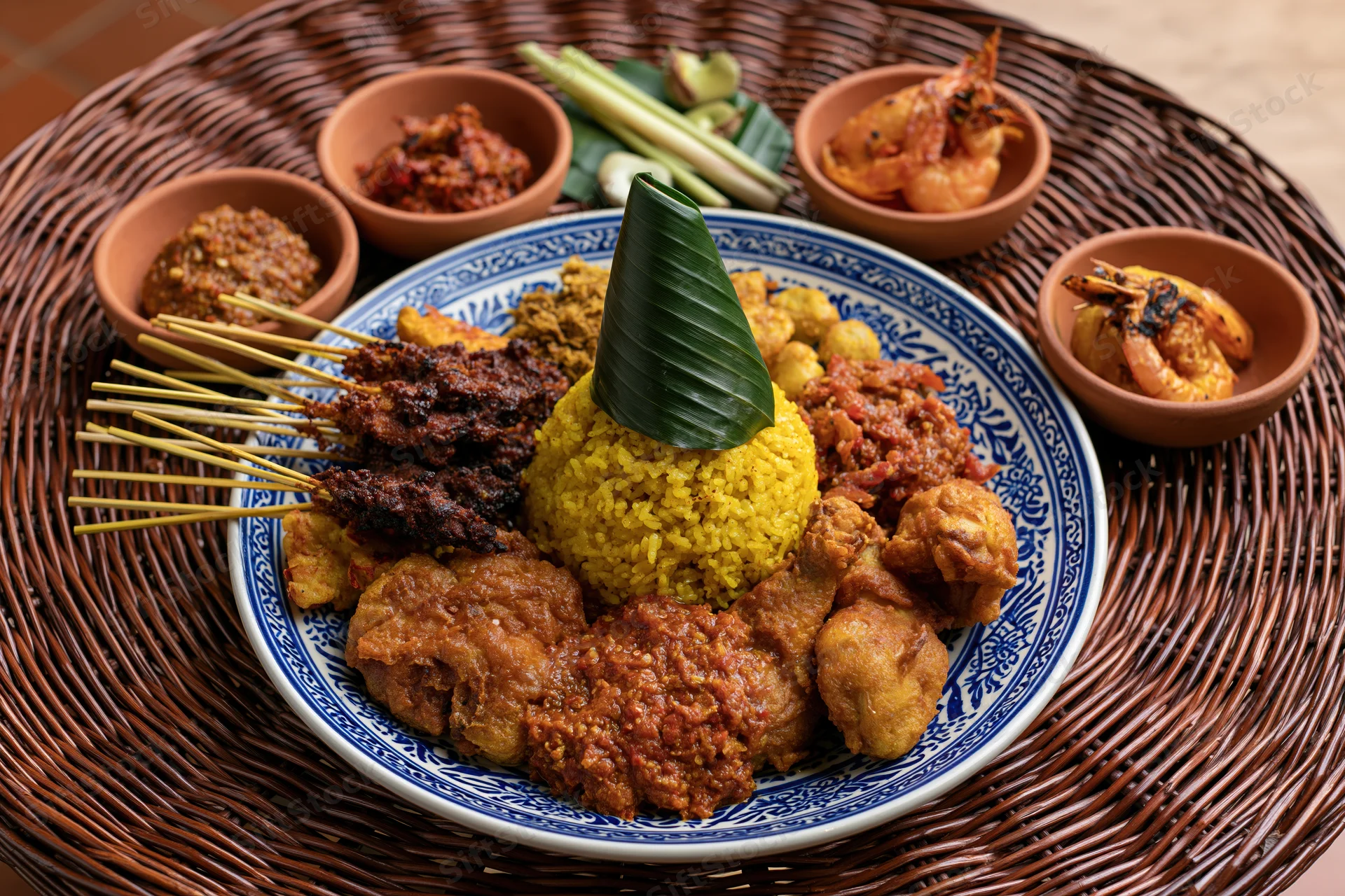 Balinese nasi kuning feast with satay, chicken, tempeh and sambal served on a blue patterned plate atop a woven rattan mat