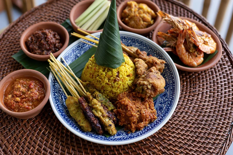 Balinese nasi kuning feast with satay and sambal on a woven rattan mat