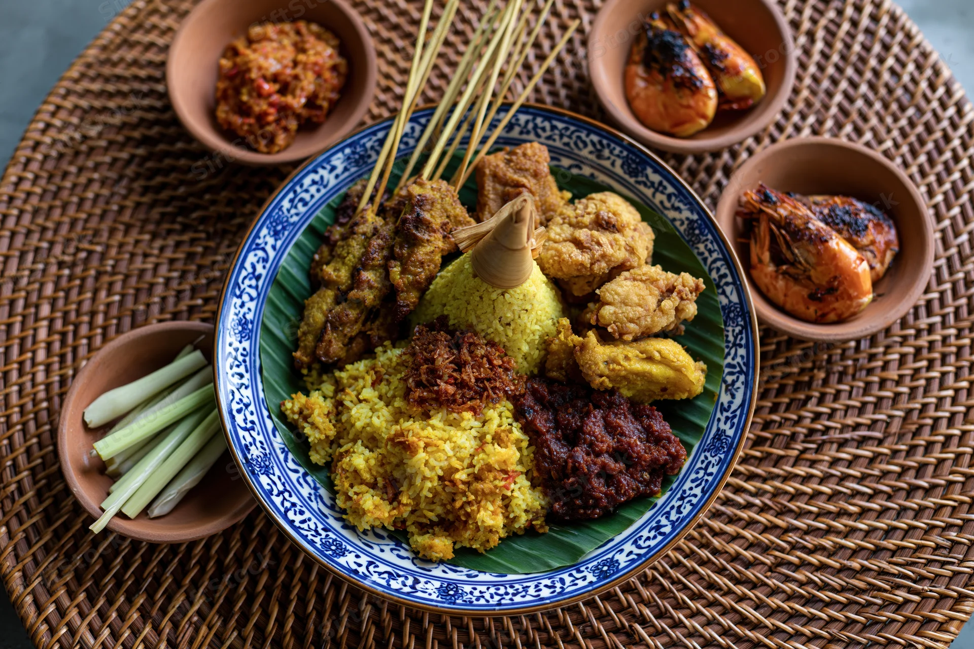Balinese nasi kuning feast with satay, grilled shrimp, and sambal served on a woven rattan mat