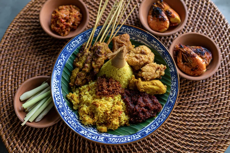 Balinese nasi kuning feast with satay, grilled shrimp, and sambal served on a woven rattan mat