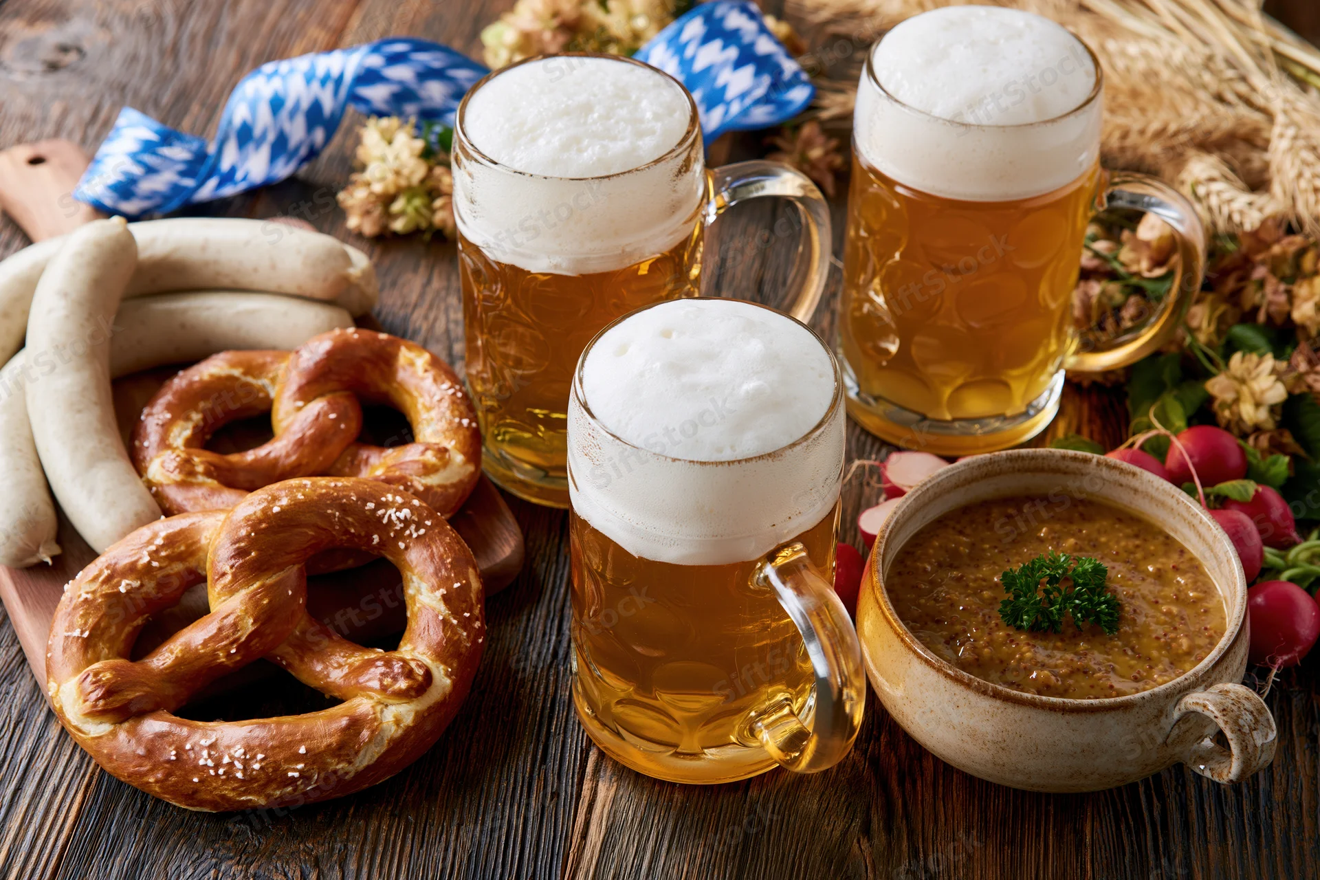 Bavarian Oktoberfest food spread with beer mugs, pretzels, sausages and soup on a dark wooden table