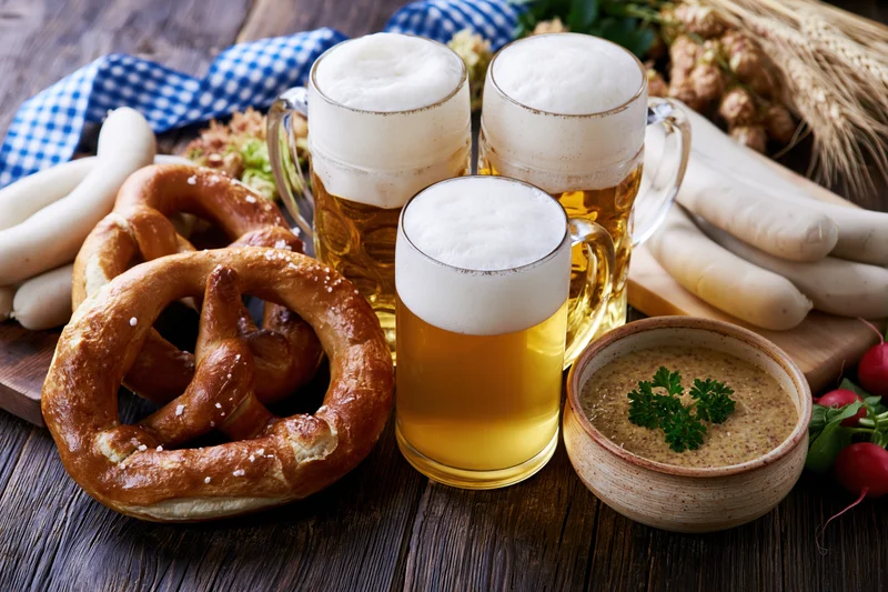 Bavarian food spread with beer, pretzels, sausages and mustard on a dark wooden table