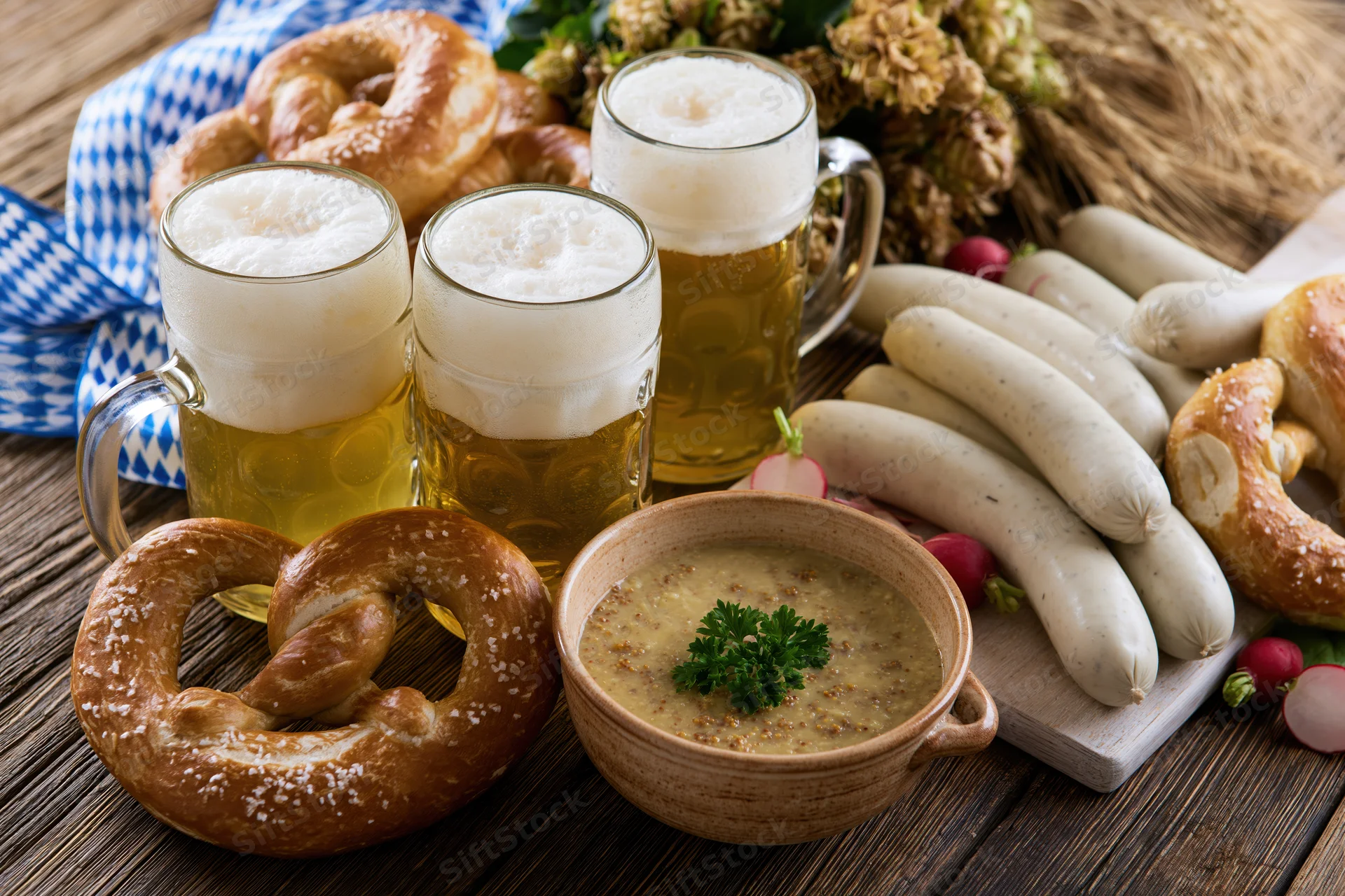 Bavarian food spread with beer mugs, pretzels, sausages and soup on a rustic wooden table