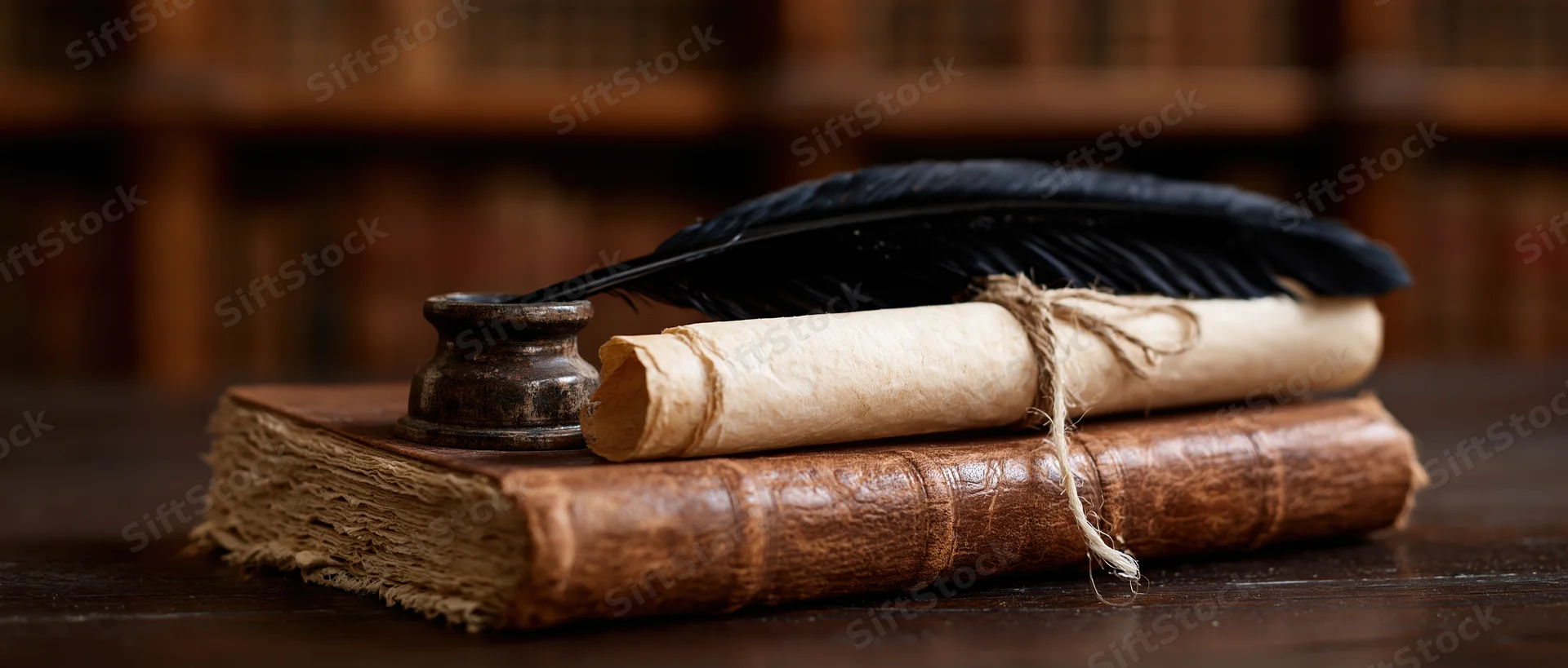 Black feather quill resting in inkwell on rolled parchment atop old leather-bound book on wooden desk in library setting