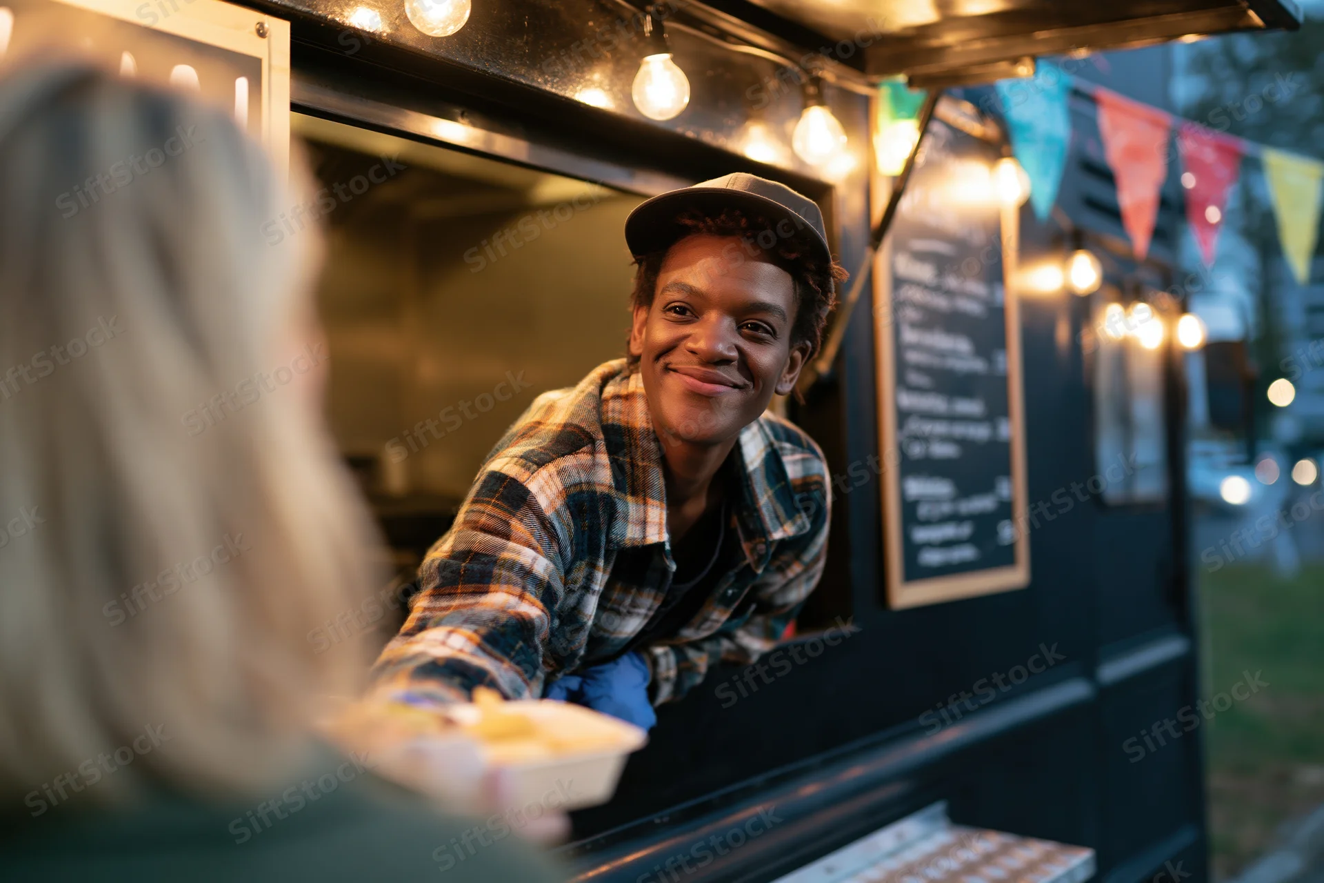 Young black man smiling while serving food from a food truck window at night