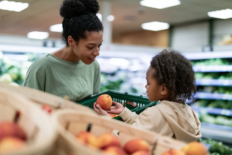 Woman and child selecting peaches in a grocery store produce section