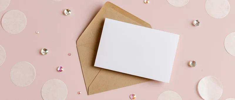 Blank white greeting card on kraft envelope with rhinestones and polka dots on pink surface