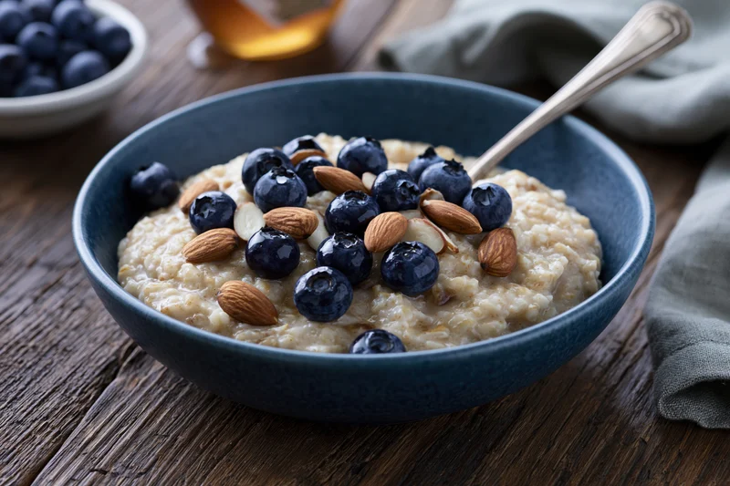 Blue ceramic bowl of oatmeal porridge topped with blueberries and almonds on wooden table
