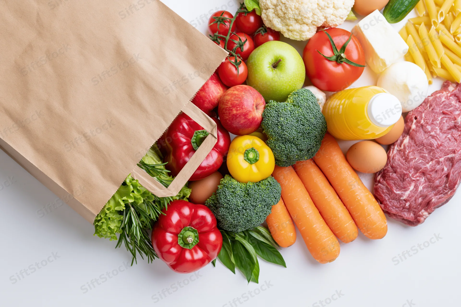 Brown paper grocery bag tipped on its side spilling fresh produce and groceries onto white surface