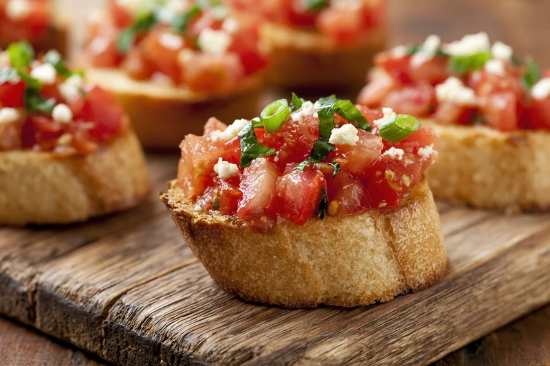 Bruschetta appetizers topped with diced tomatoes, basil, cheese and green onions on a rustic wooden cutting board