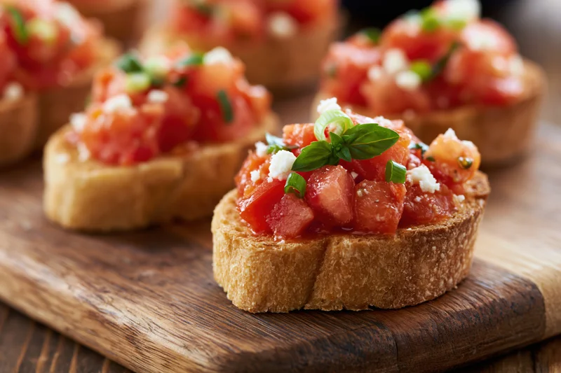 Bruschetta appetizers with tomato and basil on rustic wooden cutting board