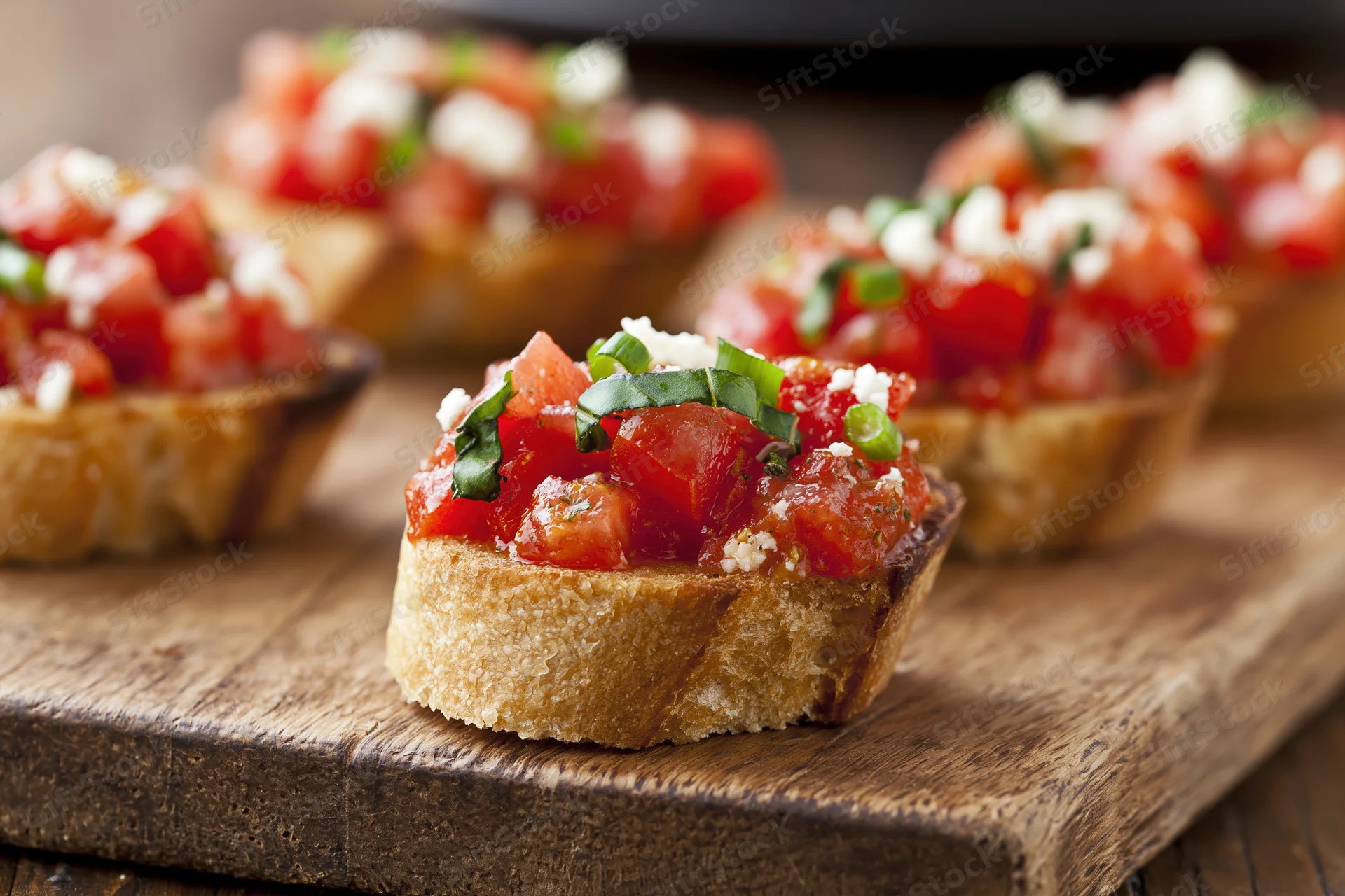 Bruschetta appetizers topped with diced tomatoes basil and cheese arranged on a rustic wooden cutting board