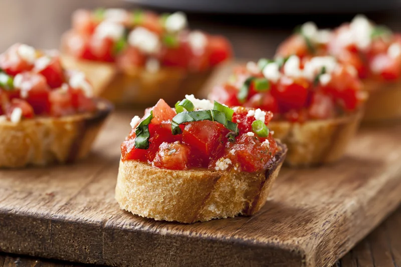 Bruschetta appetizers topped with diced tomatoes basil and cheese arranged on a rustic wooden cutting board
