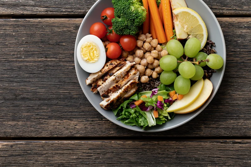 Buddha bowl with grilled chicken, vegetables, fruit and grains on a dark wooden table