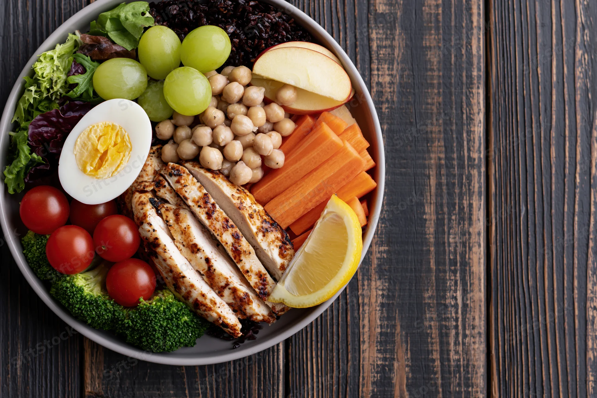 Buddha bowl with grilled chicken, vegetables, and boiled egg on a dark wooden table