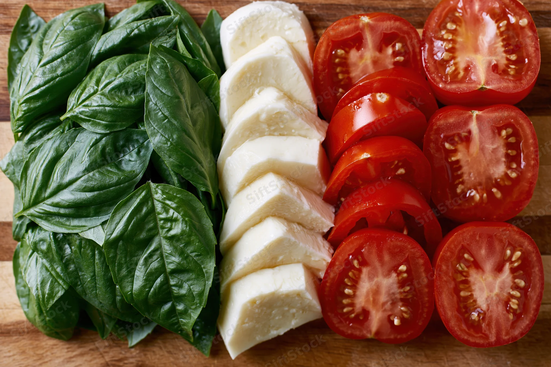 Caprese salad ingredients arranged in three parallel rows on a wooden cutting board