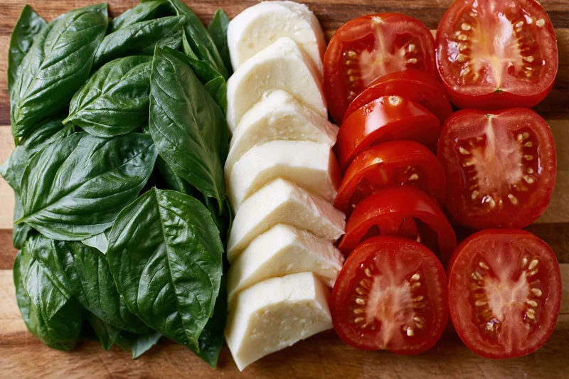 Caprese salad ingredients arranged in three parallel rows on a wooden cutting board