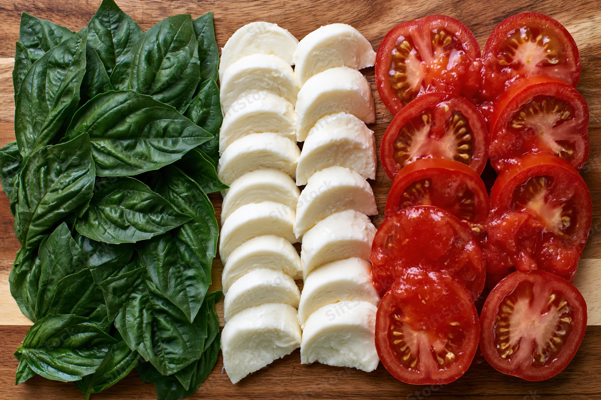 Caprese salad ingredients arranged in three parallel rows on a wooden cutting board