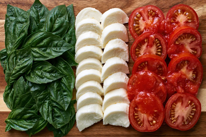 Caprese salad ingredients arranged in three parallel rows on a wooden cutting board
