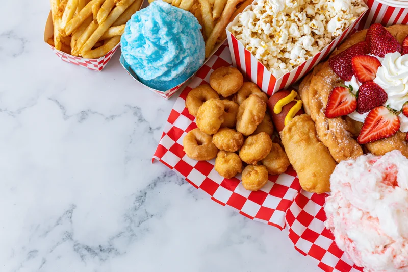 Carnival fair food spread arranged along right edge of marble countertop with red and white checkered paper containers