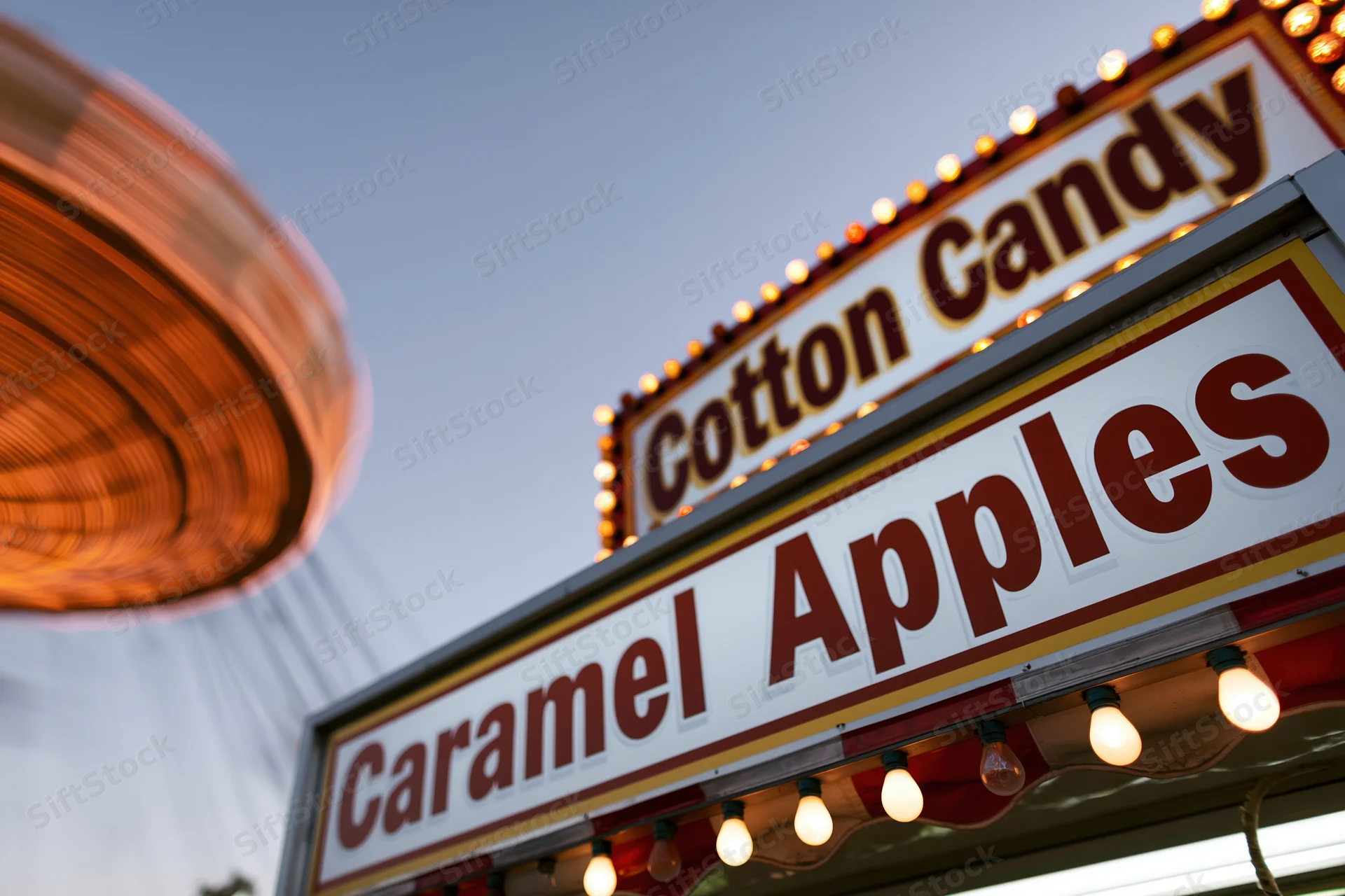 Illuminated carnival food stand signs for cotton candy and caramel apples at twilight