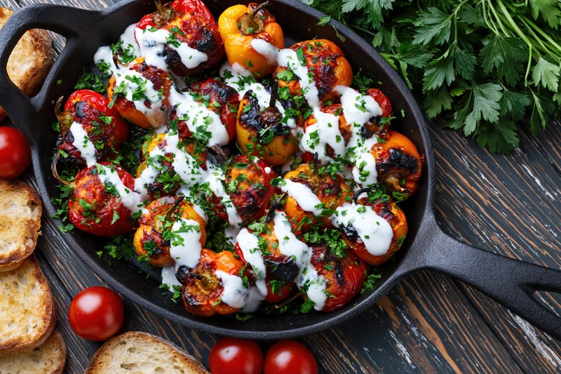 Roasted stuffed mini peppers in a cast iron skillet with creamy sauce and parsley garnish on a dark wooden table