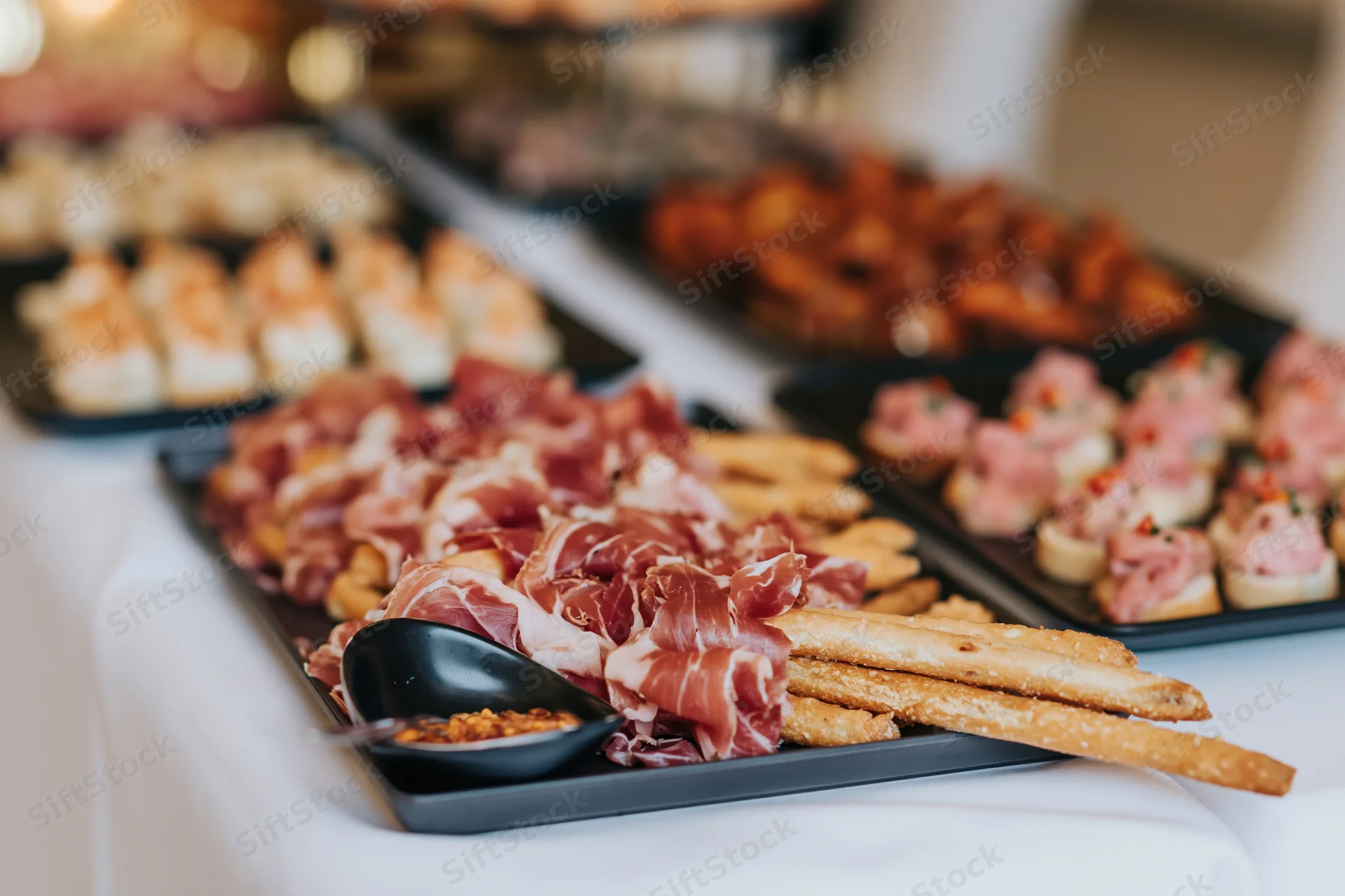 Charcuterie board with prosciutto and breadsticks on a buffet table at a reception