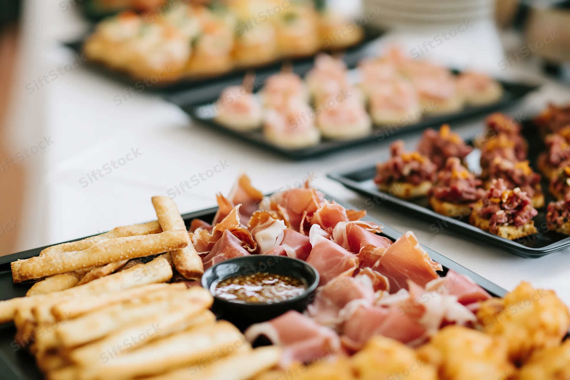 Catered buffet spread with charcuterie board and fries on black trays arranged on a white table