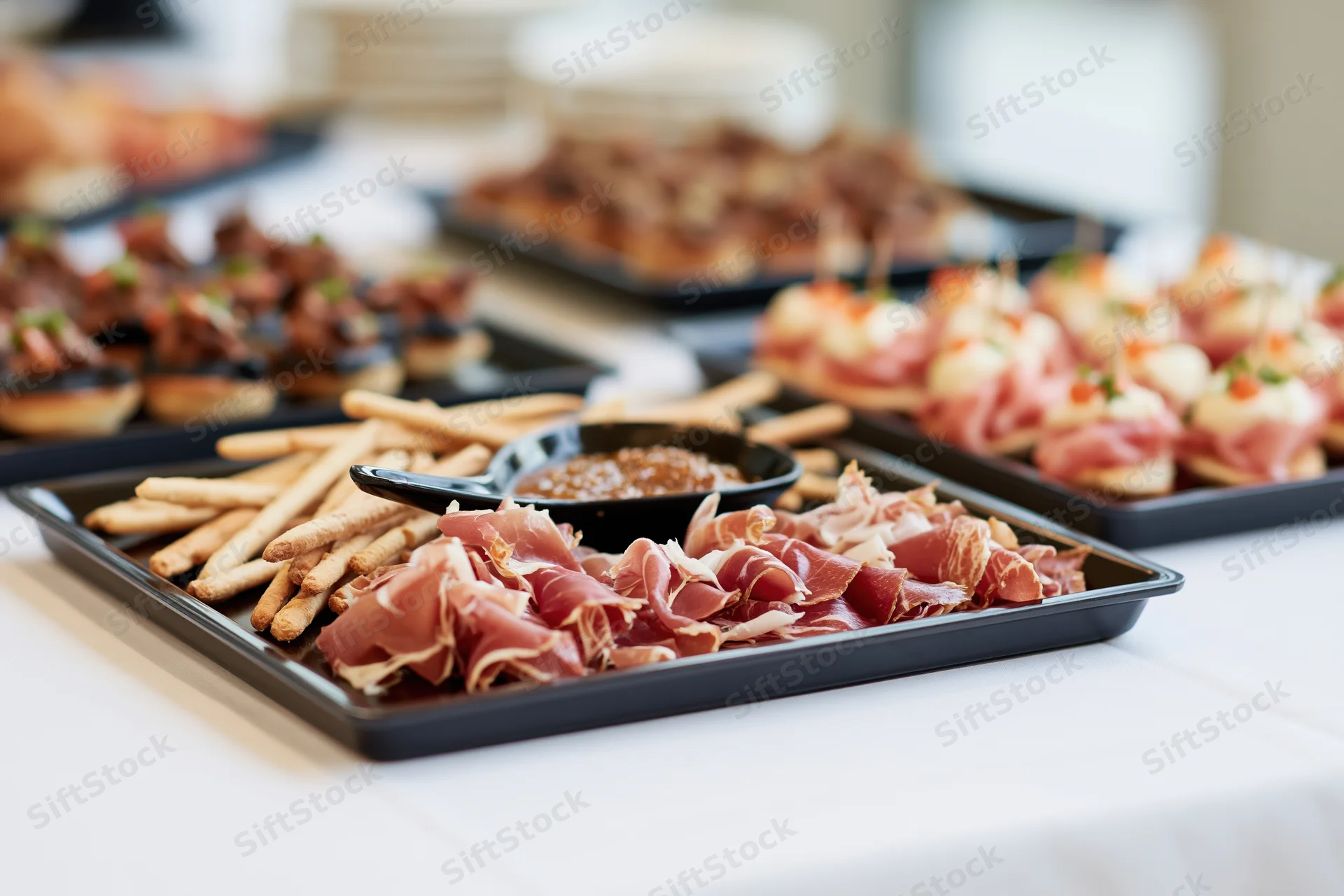 Charcuterie and appetizers arranged on black trays on a white table at a catered event