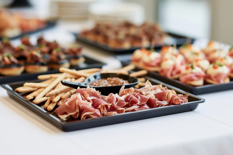 Charcuterie and appetizers arranged on black trays on a white table at a catered event
