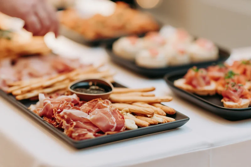 Catered buffet spread with charcuterie board and assorted appetizers on black trays on a white table