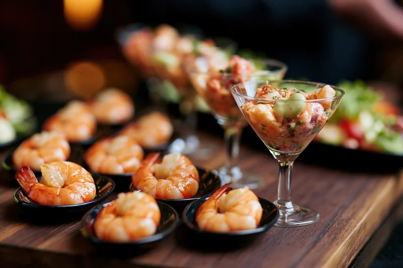 Shrimp appetizers served in black dishes and cocktail glasses on a dark wooden board