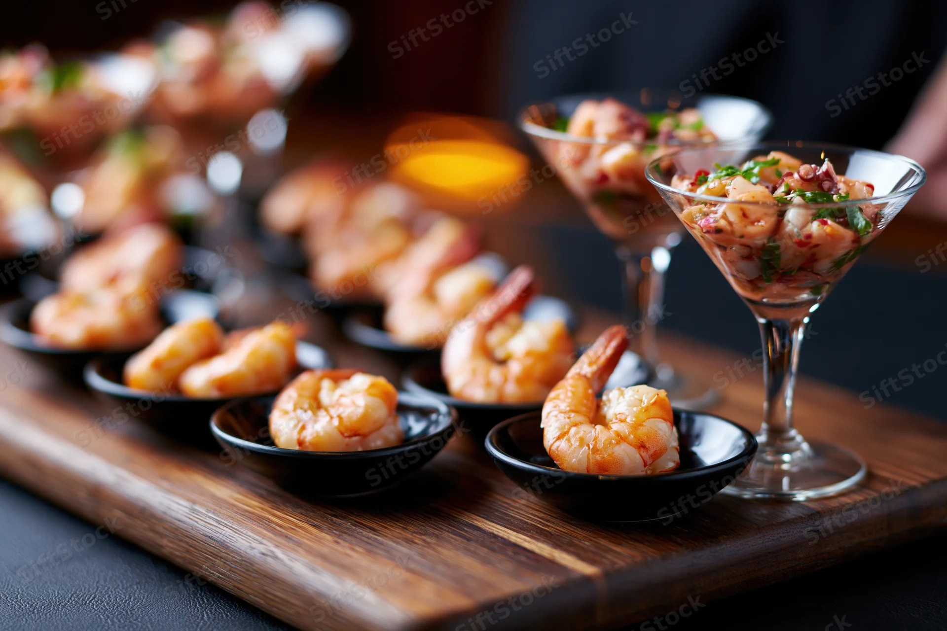 Shrimp appetizers arranged on a dark wooden board with cocktail glasses and small black bowls