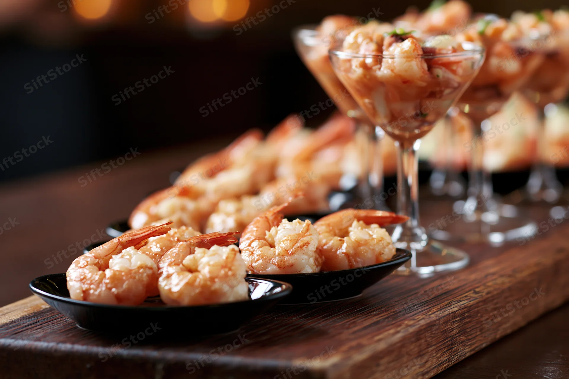 Shrimp appetizers arranged on black plates and in cocktail glasses on a dark wooden board