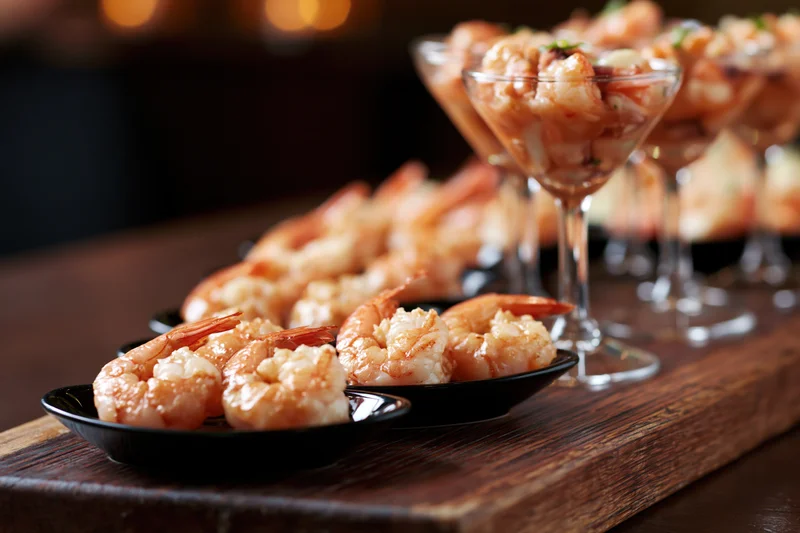 Shrimp appetizers arranged on black plates and in cocktail glasses on a dark wooden board