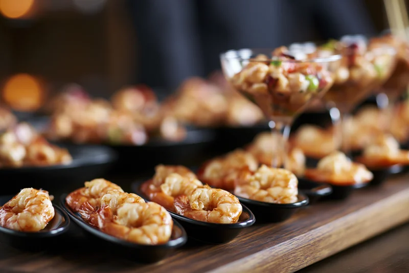 Shrimp appetizers arranged in small black bowls and martini glasses on a dark wooden board
