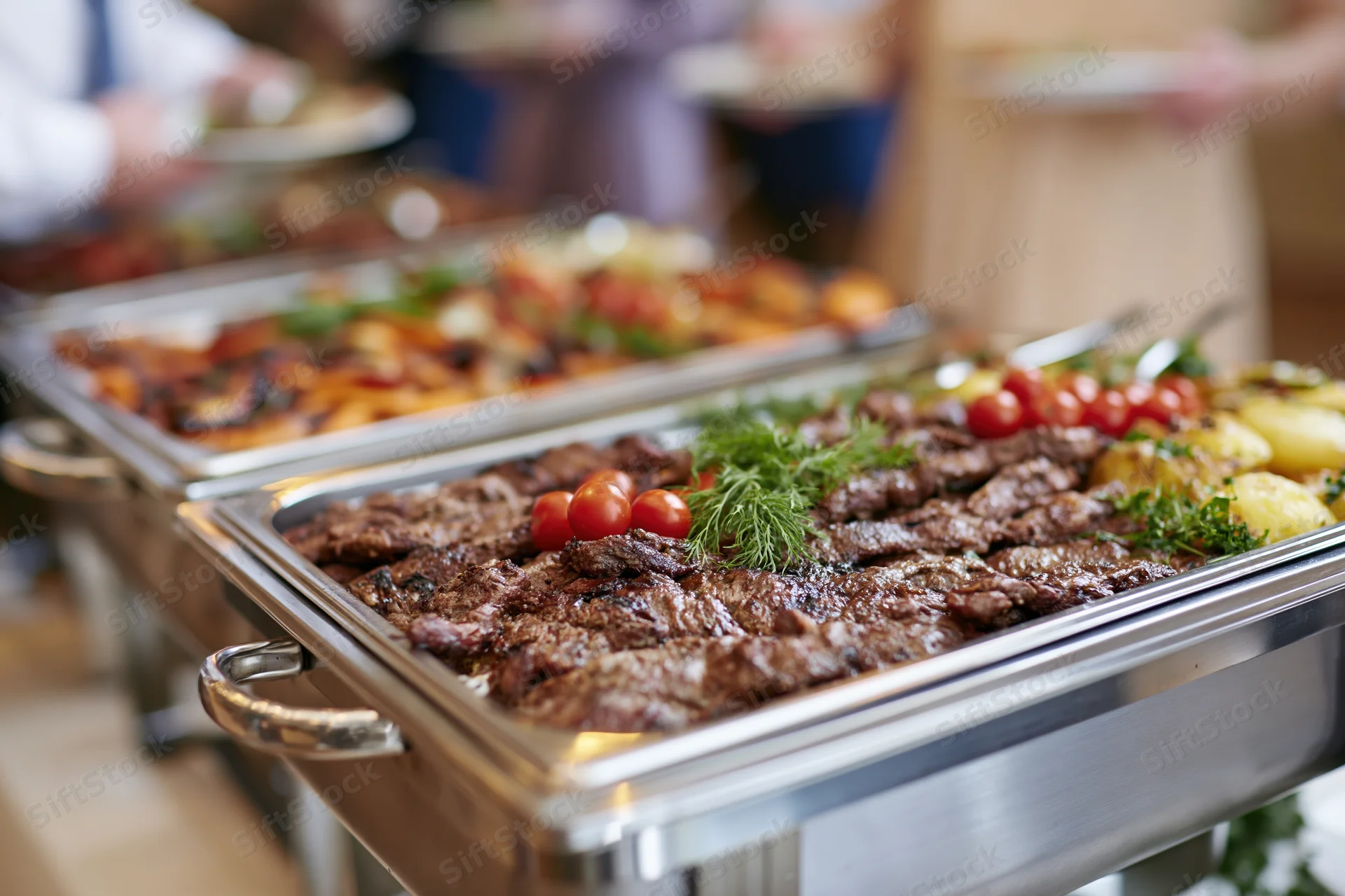 Grilled meat and roasted vegetables served on stainless steel trays at a catering buffet line