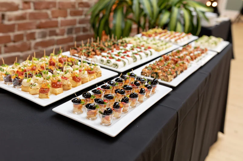 Catering buffet table with appetizers arranged on white platters covered in black tablecloth indoors