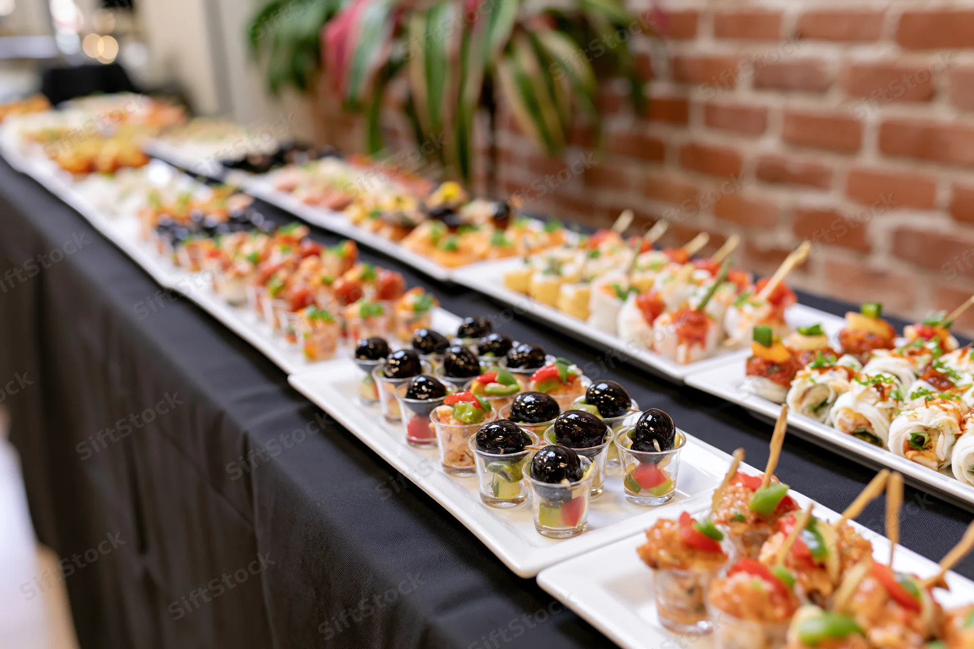 Long buffet table with assorted appetizers and sushi on white platters covered in black tablecloth