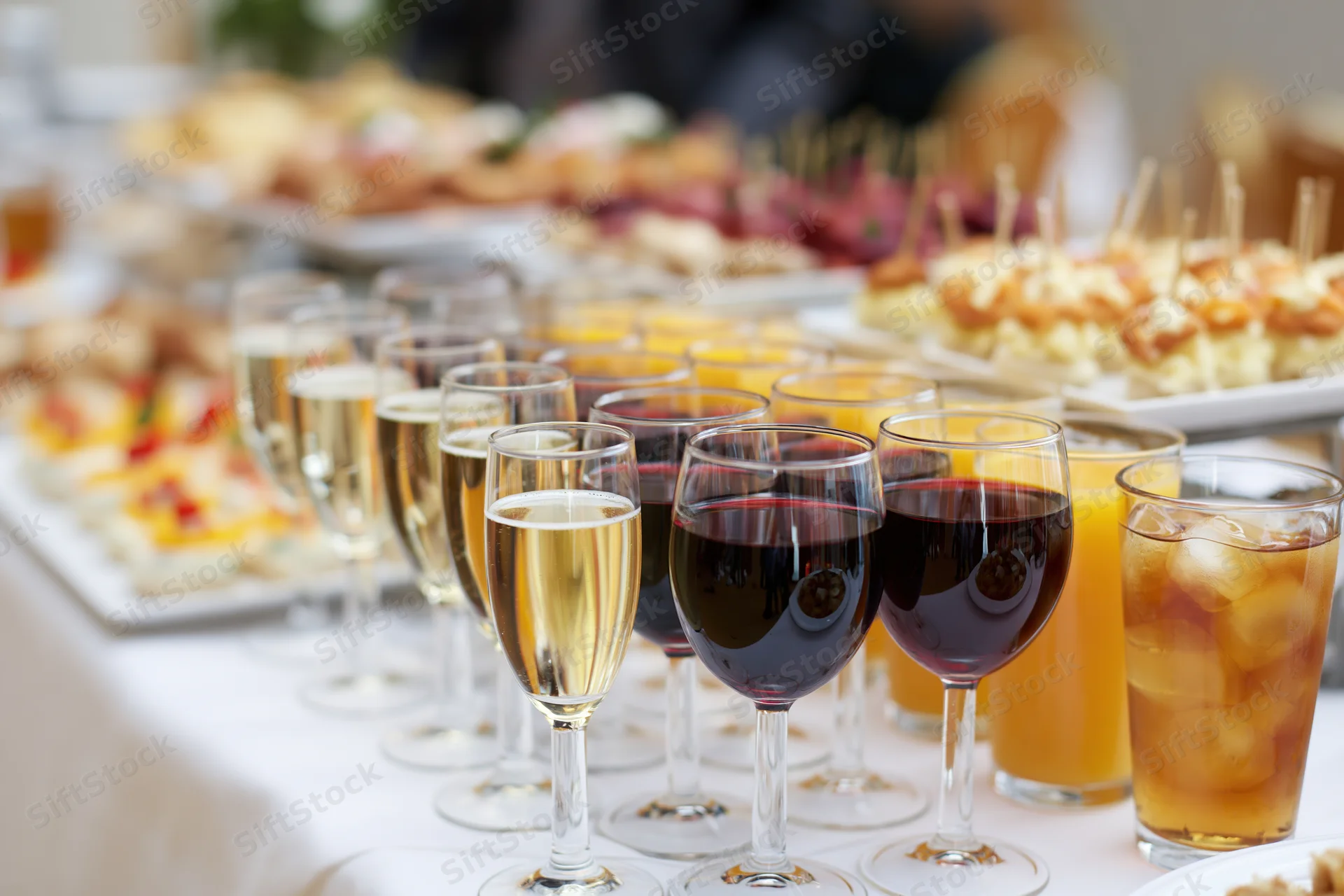 Rows of wine and champagne glasses lined on a buffet table with appetizers in the background