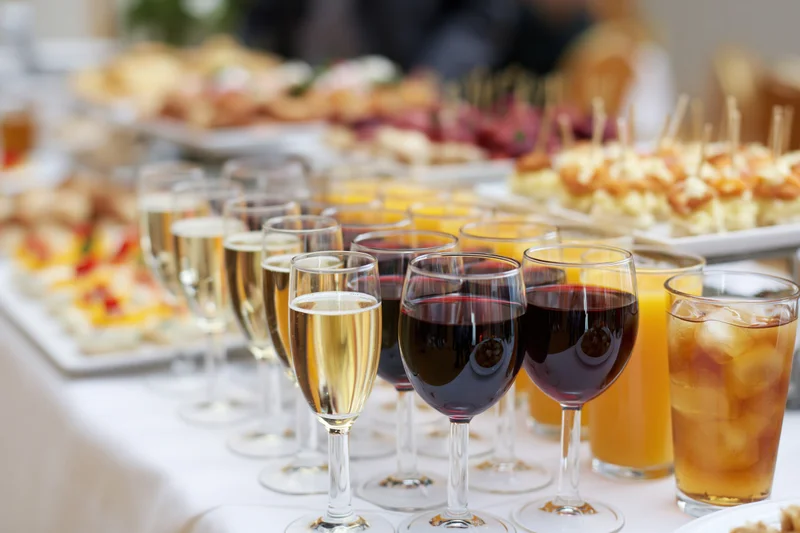 Rows of wine and champagne glasses lined on a buffet table with appetizers in the background