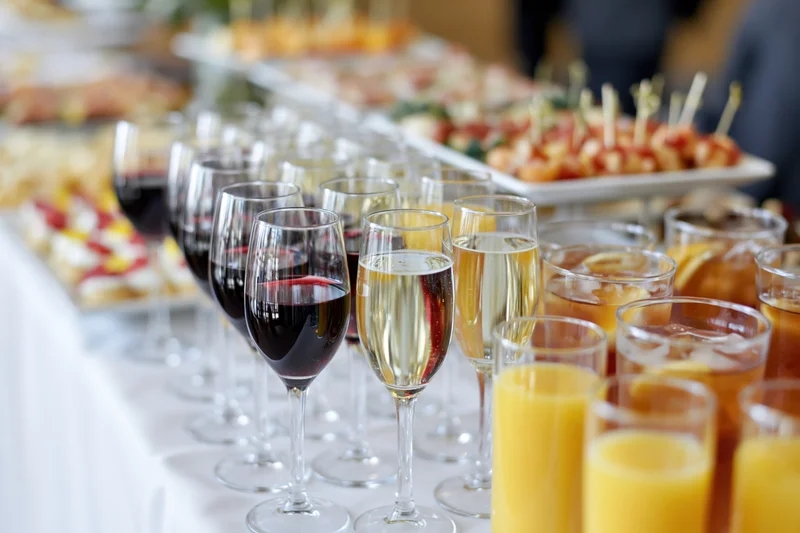 Rows of wine and champagne glasses on a buffet table with appetizers in the background