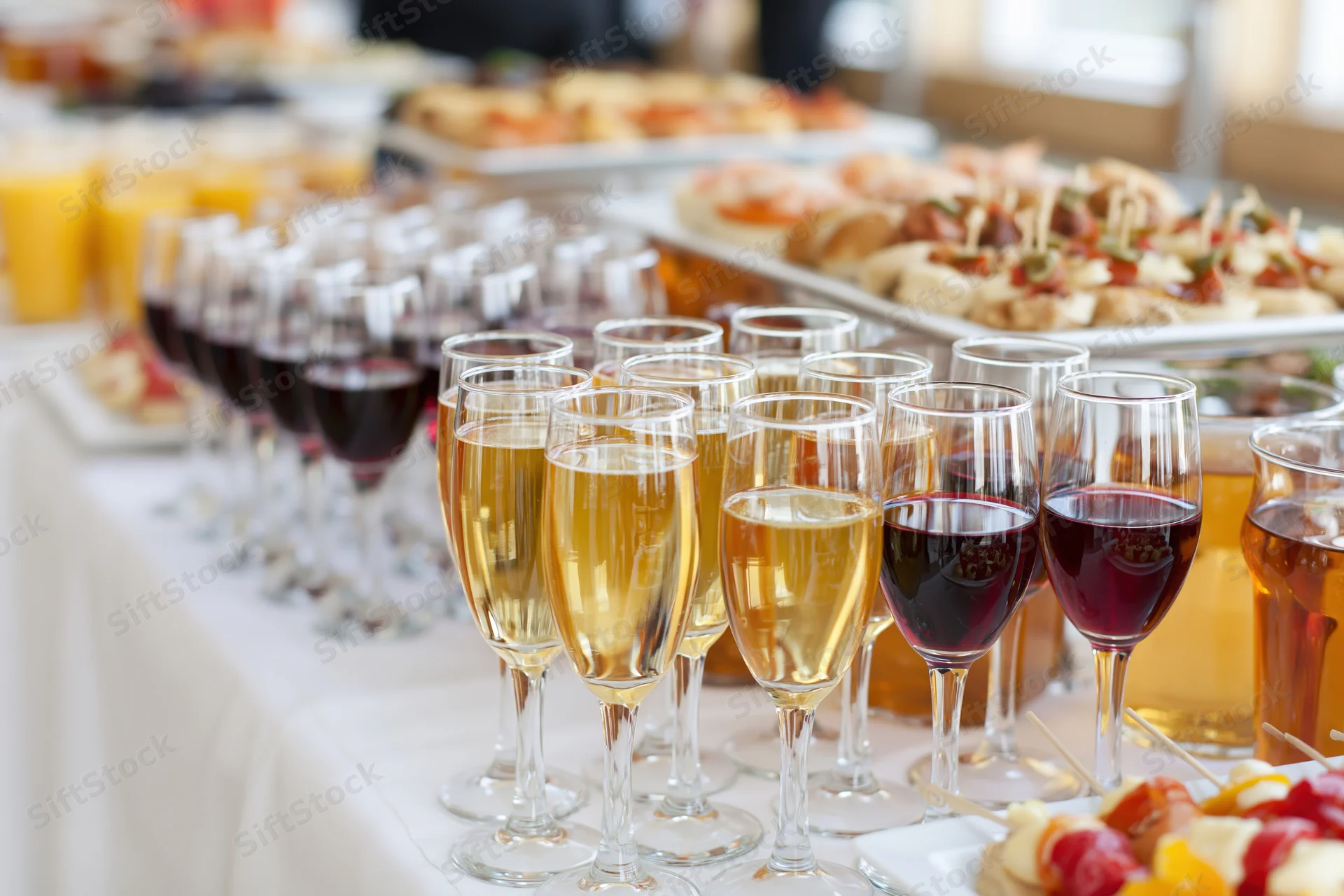 Rows of champagne and wine glasses on a buffet table with appetizers and platters in the background