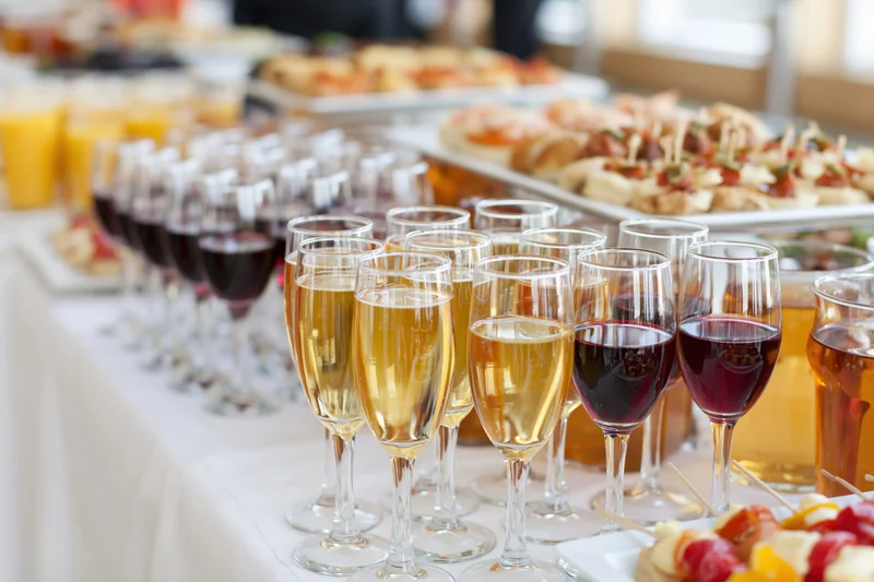 Rows of champagne and wine glasses on a buffet table with appetizers and platters in the background