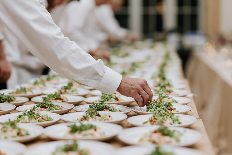 Catering staff garnishing rows of plated salads on a long table