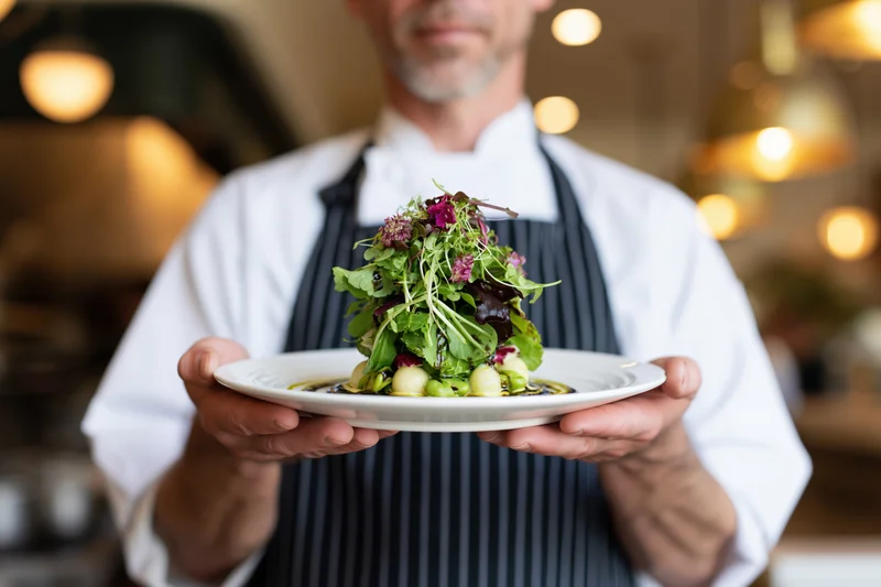 Chef holding a plated salad with greens and edible flowers in a restaurant kitchen