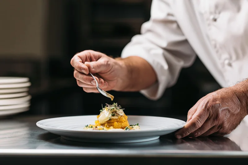 Chef drizzling sauce over plated dish in restaurant kitchen